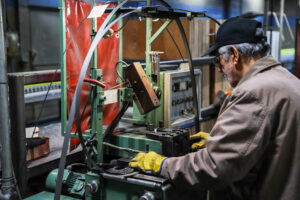 man with white hair, wearing a black hat and yellow gloves, working at a green machine