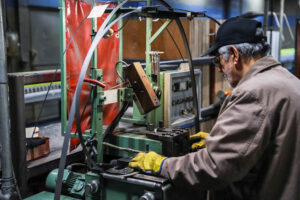 man with white hair, wearing a black hat, working at saw machine