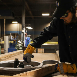 man in safety glasses and a black hat working with blades at a wrokstation
